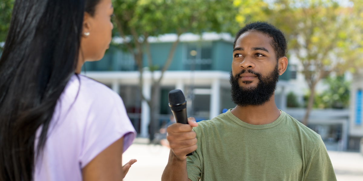 Afrikanischer Radiojournalist interviewt eine Person im Freien.