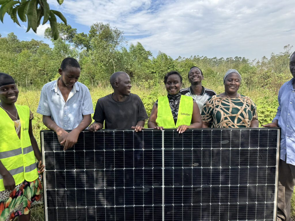 Shifra Ainomugisha mit einer Gruppe von Landwirt*innen und einem Solarpanel in Uganda.